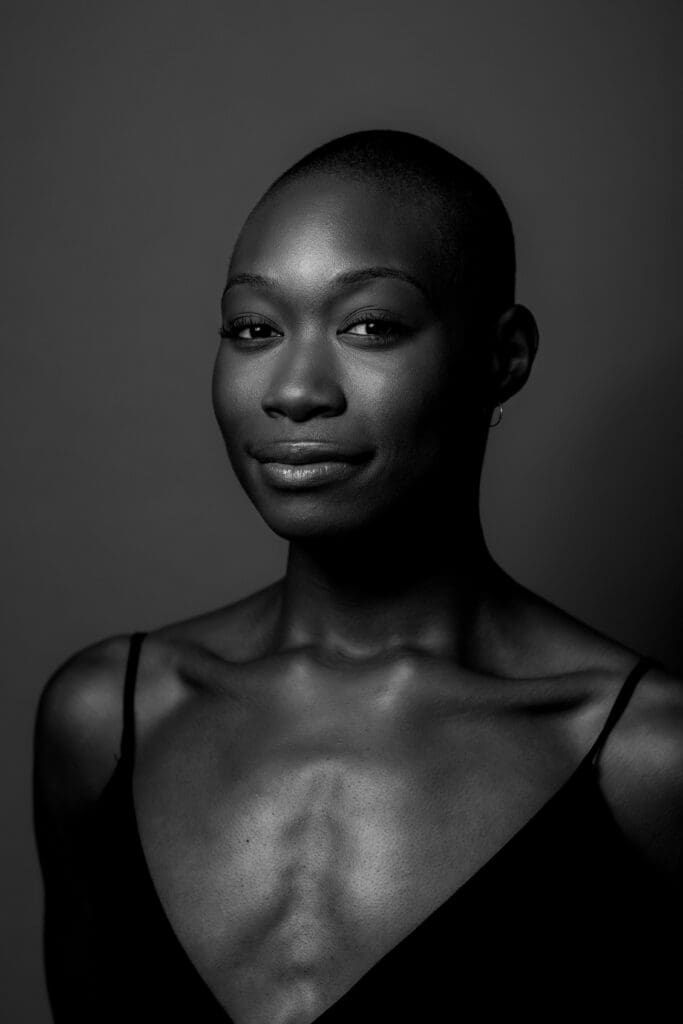 Black and white portrait photo of Nayaa Opong. They are smiling slyly looking into the camera, wearing a black top.