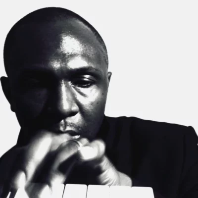 Black and white headshot of HPRIZM. They are playing a small keyboard wearing a black top.