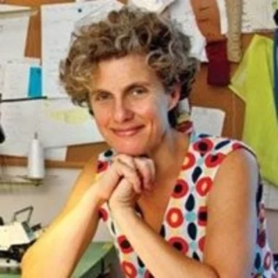 Color headshot of Liz Prince. They are in their office wearing a red and white patterned dress, their head resting on their clasped hands.