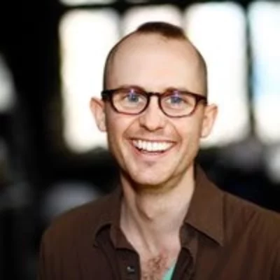 Color headshot of Solomon Weisbard. They are smiling at the camera, wearing brown glasses and a brown collared shirt.