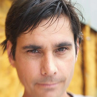 Color photo portrait of Ted Coffey. They are against a yellow background, and the image has a motion blur around the edges.