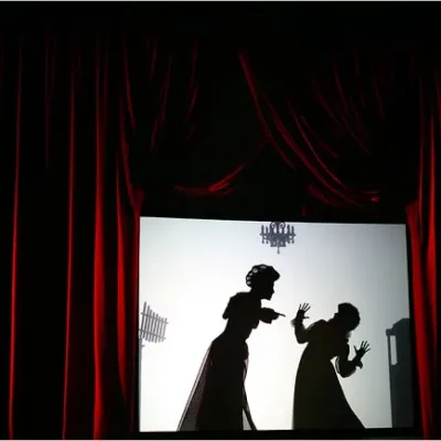 A silhouette of two people arguing is framed by red velvet curtains
