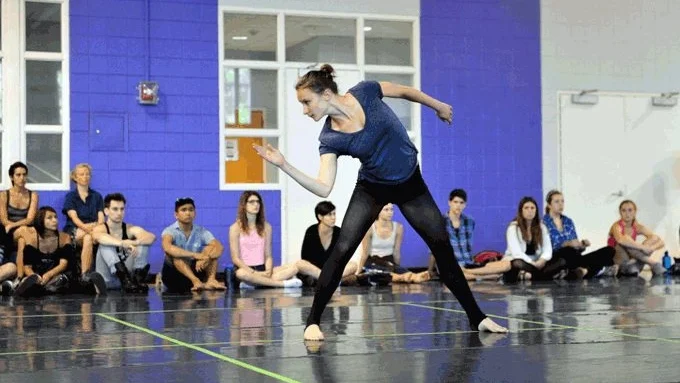 A woman dancing in front of studio class that is sitting around her.
