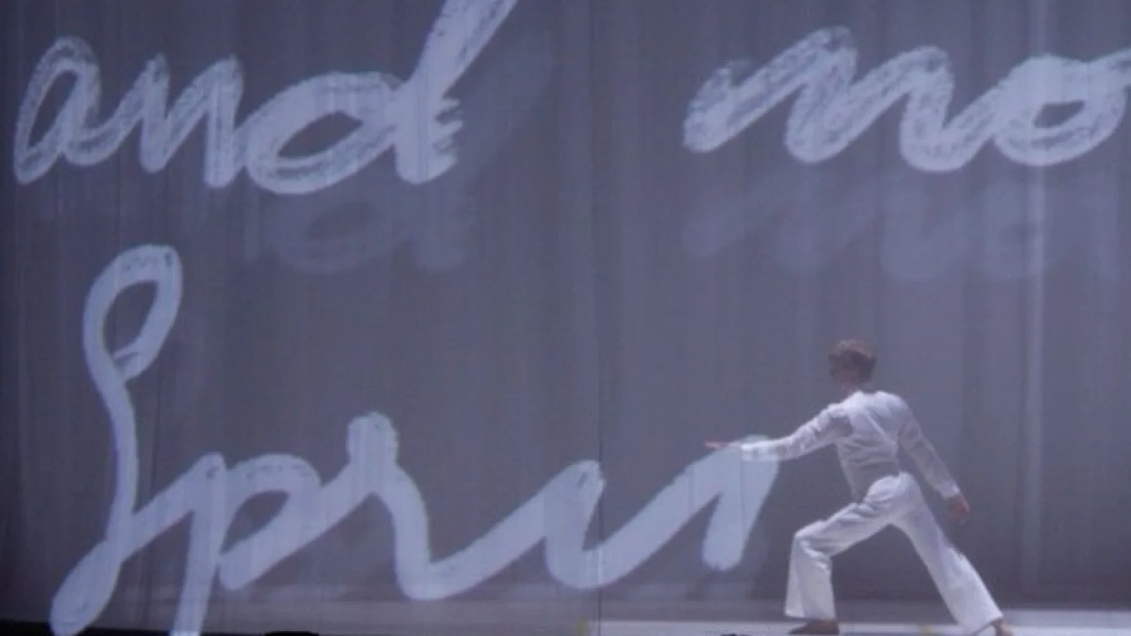 A dancer performs on a stage with huge images of handwriting projected behind them